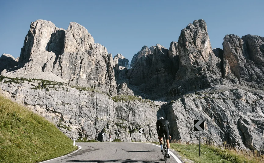 Ciclista pedala in salita su strada curva davanti a scogliere ripide