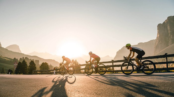 Drei Radfahrer fahren bei Sonnenaufgang auf einer Bergstraße