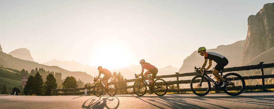 Three cyclists riding on a mountain road at sunrise