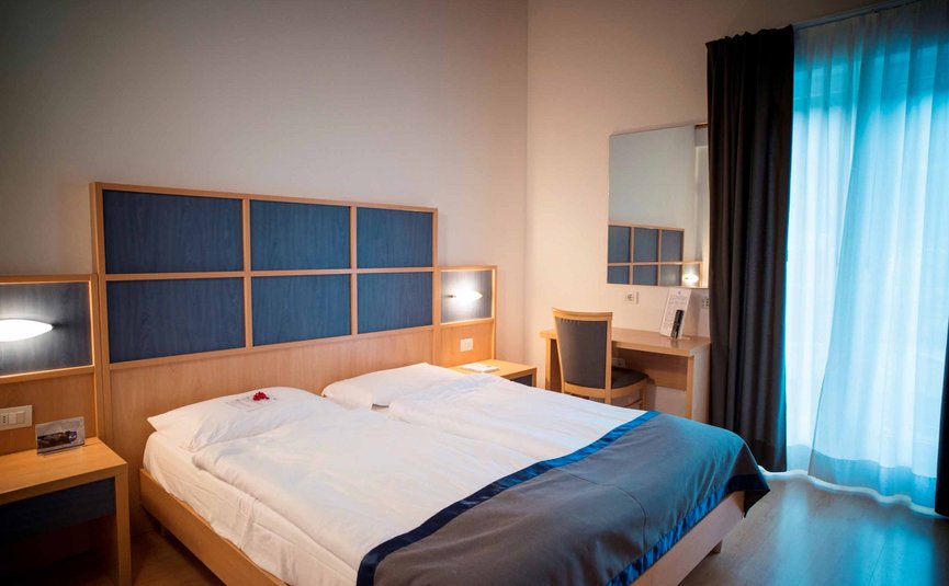 Modernes Hotelzimmer mit Doppelbett, Schreibtisch und Vorhängen am Fenster