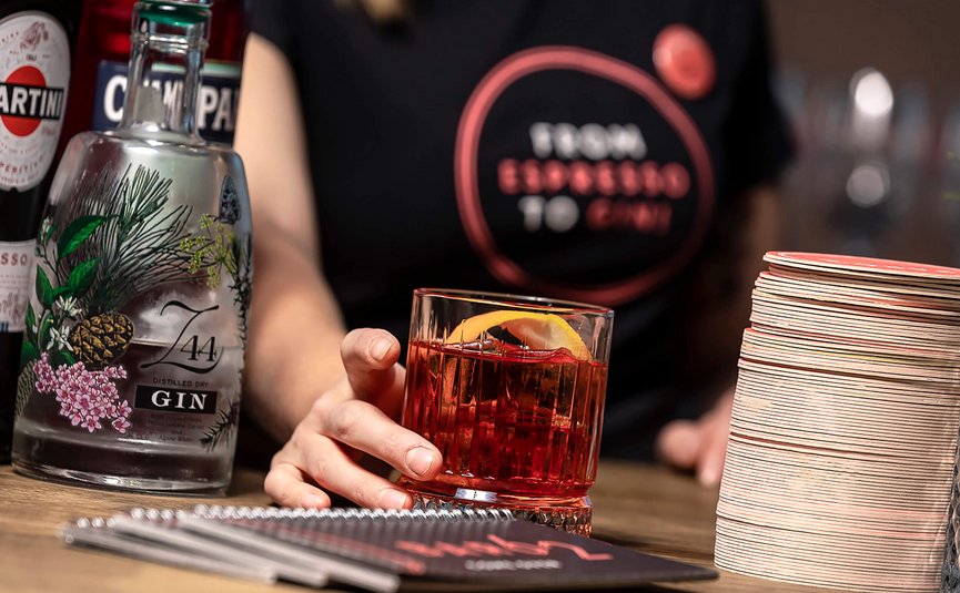 Mano che tiene cocktail Negroni vicino a bottiglie di gin e Martini