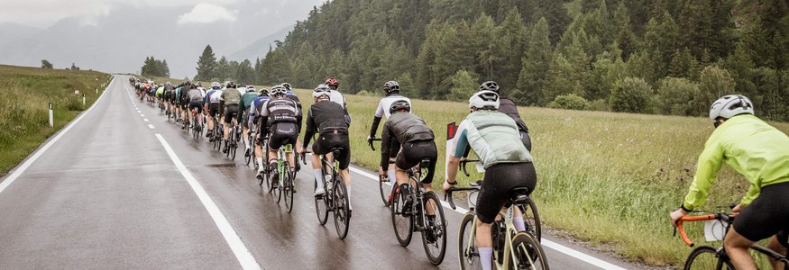 Cyclists riding on wet country road surrounded by forested hills