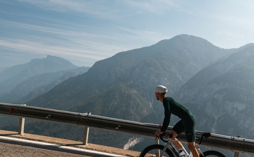 Ciclista che pedala in salita su strada asfaltata con montagne sullo sfondo