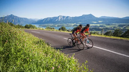 Ein Rennrad-Wochenende im SalzburgerLand – Salzkammergut © Heiko Mandl Zwei Radfahrer fahren auf einer Landstraße mit Bergen und See im Hintergrund