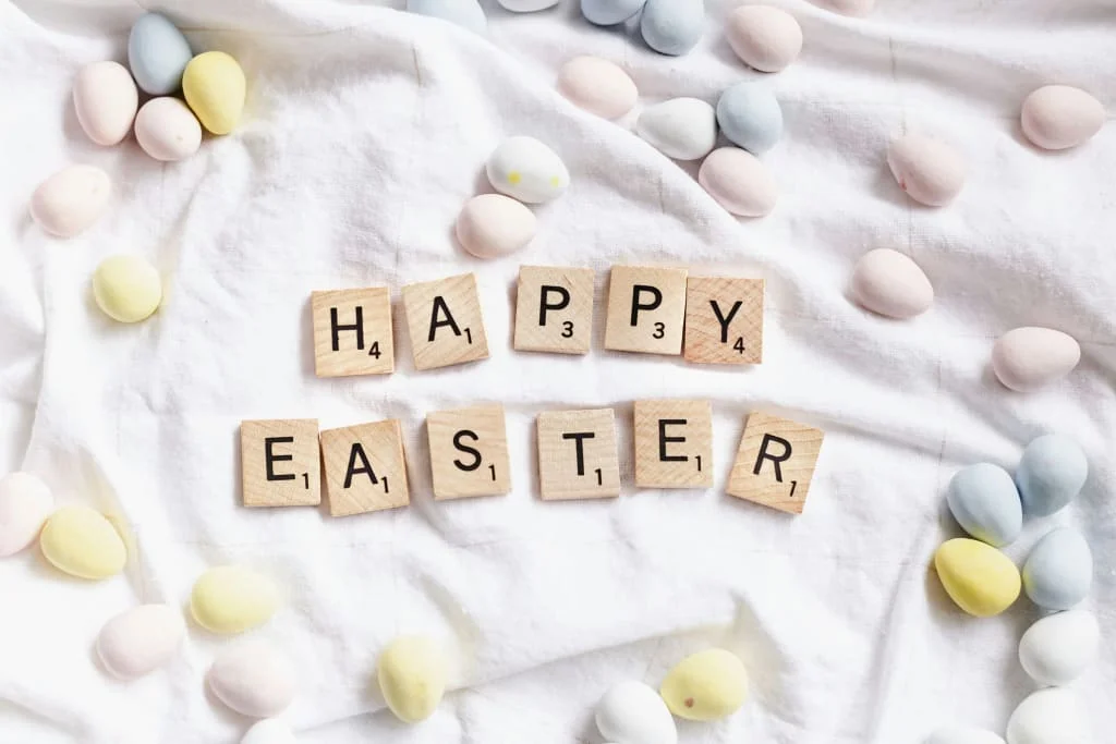 Scrabble-Buchstaben bilden den Schriftzug Frohe Ostern auf weißem Tuch mit bunten Eiern