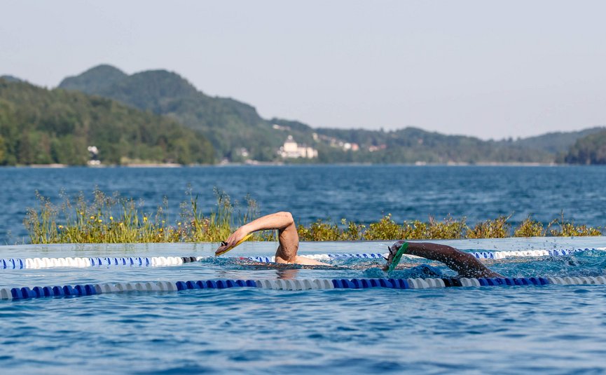 Two swimmers in outdoor pool with mountains in the background