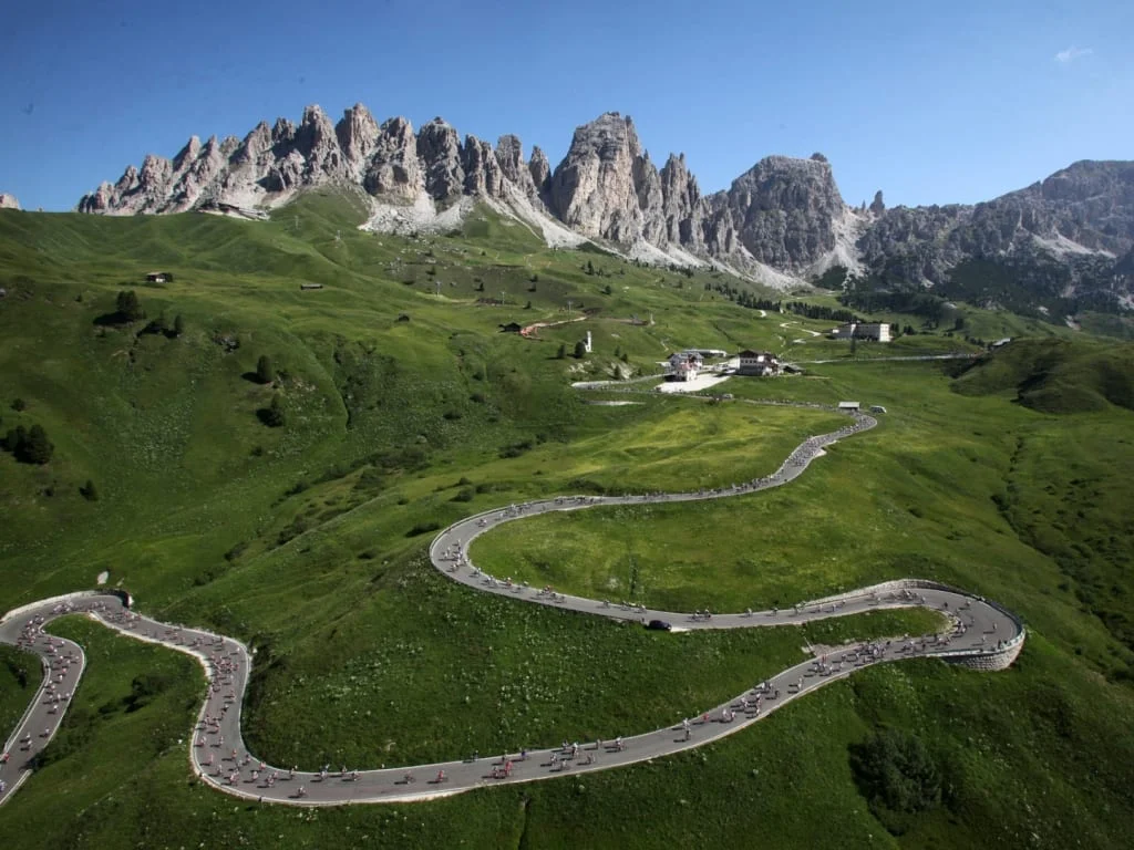 Kronkelende bergweg met fietsers en rotsachtige pieken op de achtergrond