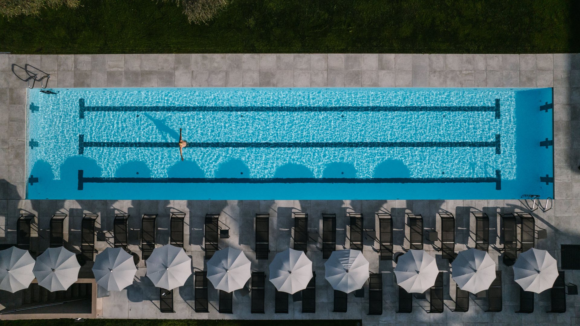 Triathlon Hotels: Deine Base für Training & Erholung © Edelbaur Media Luftaufnahme eines Schwimmbeckens mit Person und Liegestühlen mit Sonnenschirmen