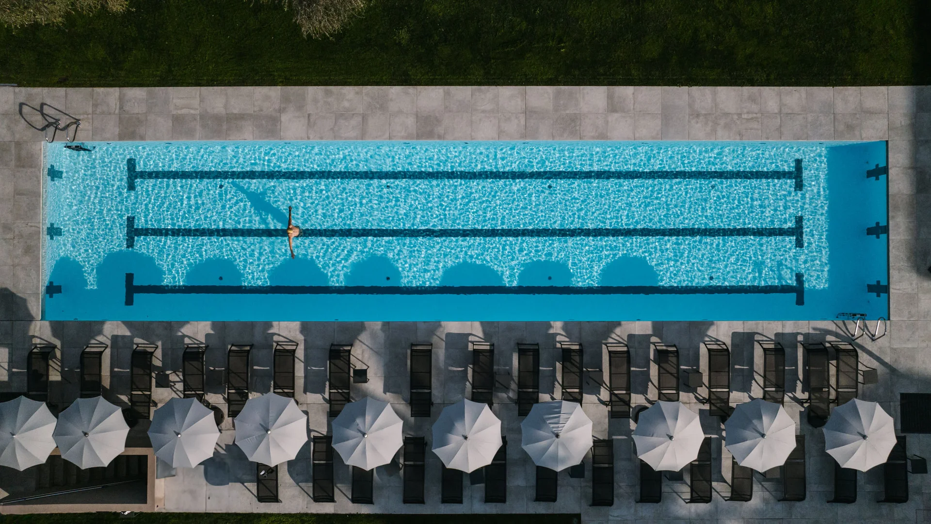 Aerial view of a swimming pool with person and sun loungers with umbrellas