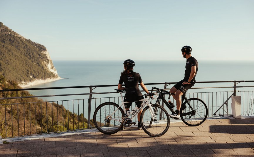 Due ciclisti ammirano la vista sul mare da un belvedere.