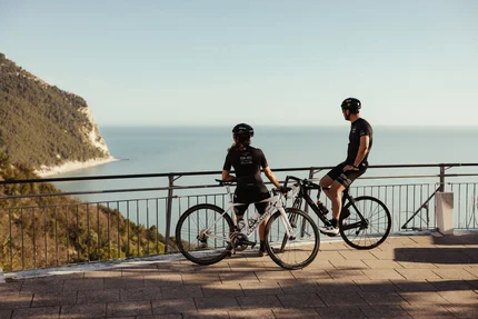 Zwei Radfahrer genießen den Blick auf das Meer von einer Aussichtsplattform.