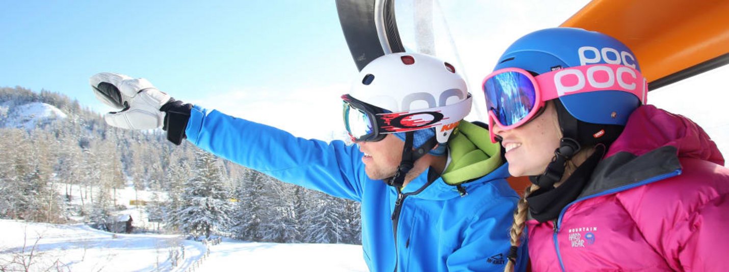 Twee skiërs in gondel, man wijst naar besneeuwd berglandschap