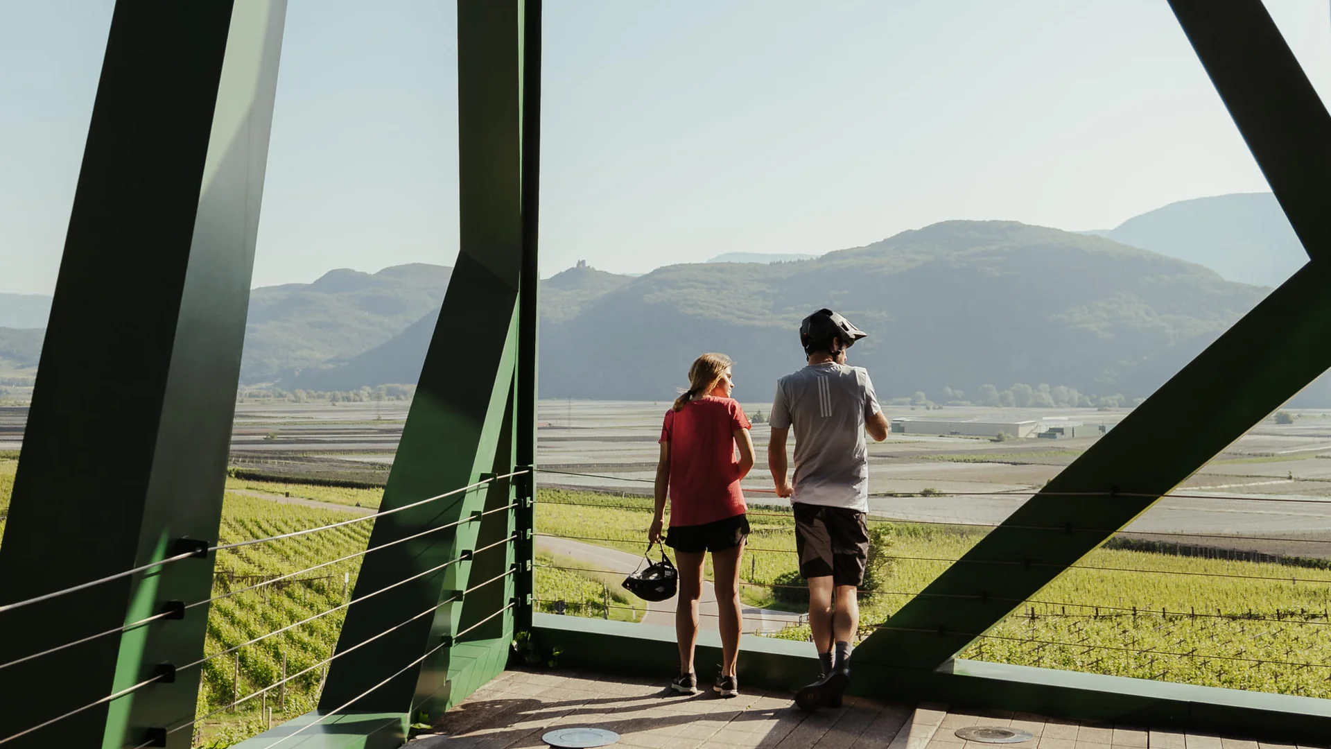Golden autumn on the road bike in Tramin Two people view a vineyard landscape from a modern observation deck
