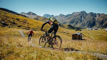 Zwei Mountainbiker fahren auf einem Pfad in den Bergen bei klarem Himmel