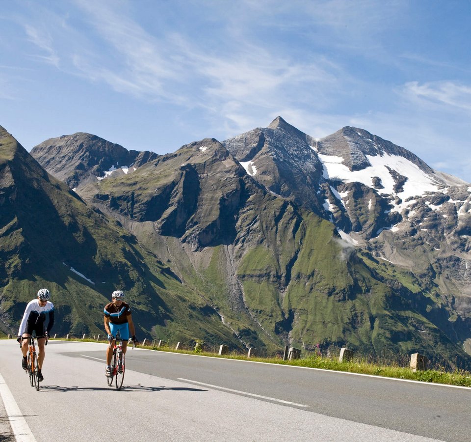 Glocknerkönig © Heiko Mandl Zwei Radfahrer auf Bergstraße mit schneebedeckten Gipfeln im Hintergrund