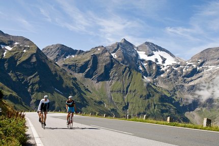 Glocknerkönig © Heiko Mandl Zwei Radfahrer auf Bergstraße mit schneebedeckten Gipfeln im Hintergrund