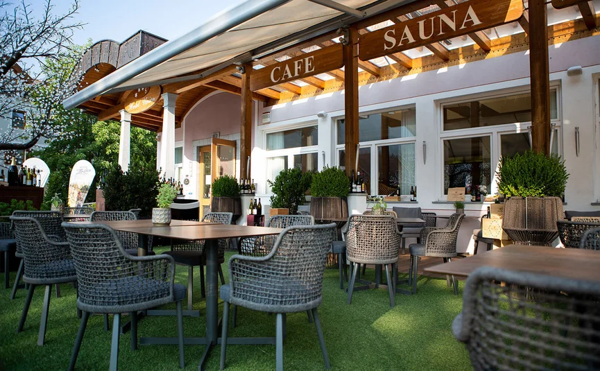 Terrasse eines Cafés mit Stühlen und Tischen im Freien unter Holzüberdachung