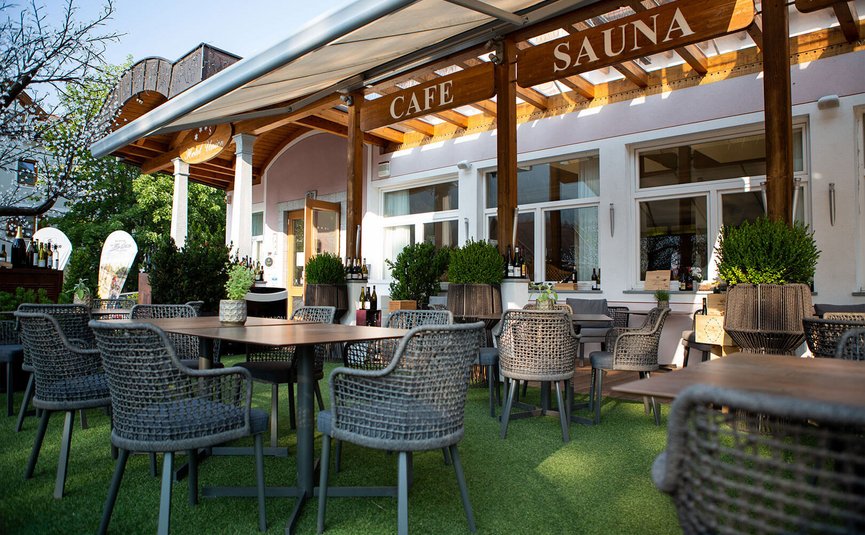 Terrasse eines Cafés mit Stühlen und Tischen im Freien unter Holzüberdachung