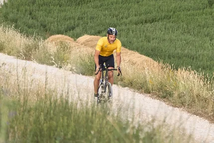 Radfahrer fährt auf geschwungenem Weg durch grünes und gelbes Landschaftsfeld
