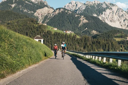Zwei Radfahrer fahren auf Bergstraße mit grünen Hügeln und Bergen im Hintergrund