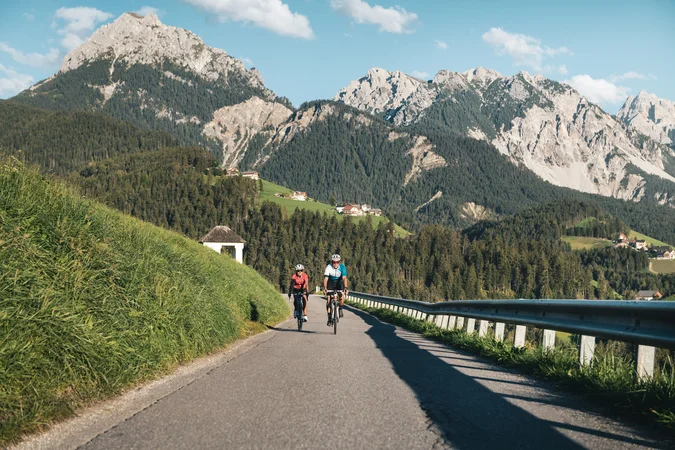 Roadbike Holidays © Alex Moling Zwei Radfahrer fahren auf Bergstraße mit grünen Hügeln und Bergen im Hintergrund