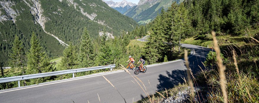 Tannheimer Tal © Christina Neubauer Zwei Radfahrer fahren auf Bergstraße in bewaldeter Alpenlandschaft bei klarem Himmel