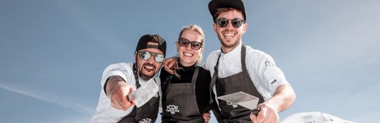 Drie lachende koks met schorten en zonnebrillen voor besneeuwde berg