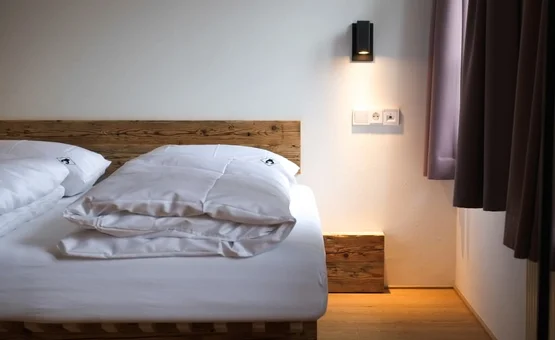 Gemachtes Bett mit weißen Decken und Holzkopfteil in schlichtem Schlafzimmer