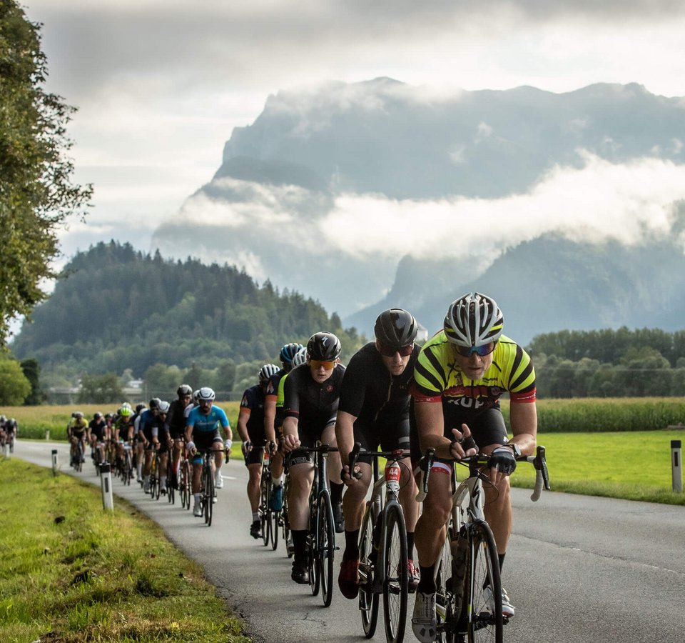 Radfahrer fahren in einer Gruppe auf einer Landstraße vor Bergen und Wolken