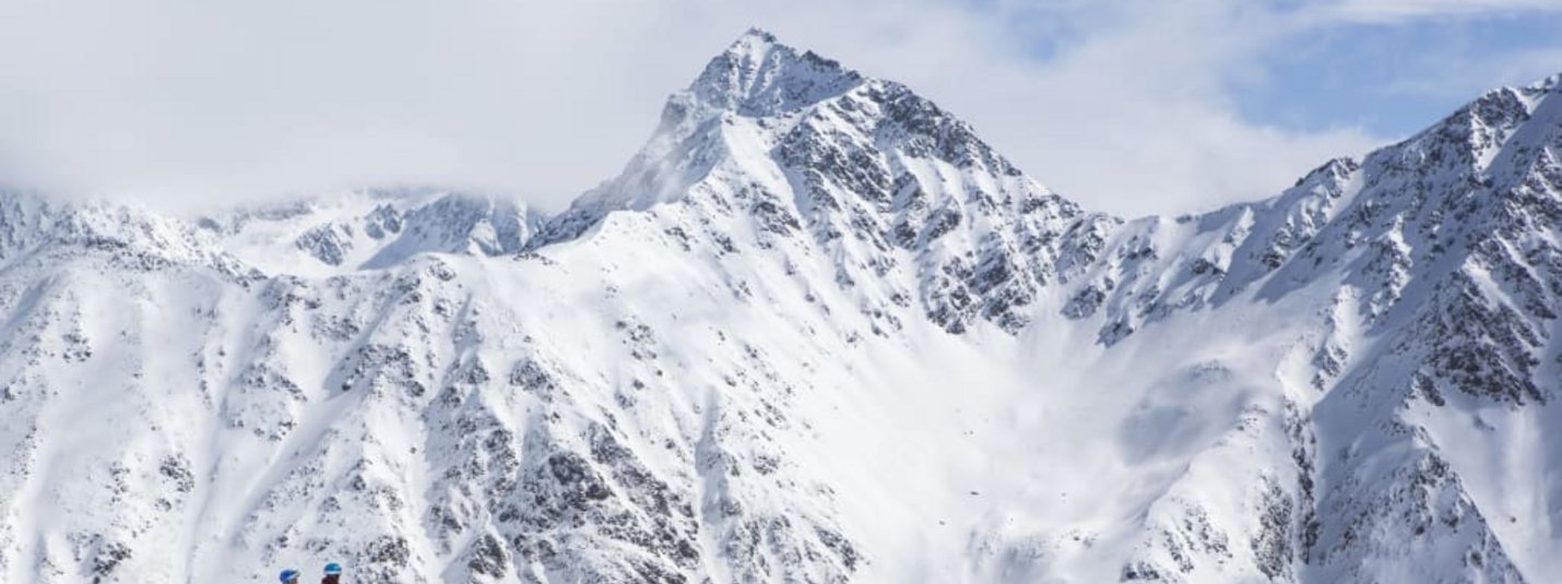 Zwei Skifahrer stehen vor verschneiten Berggipfeln unter blauem Himmel