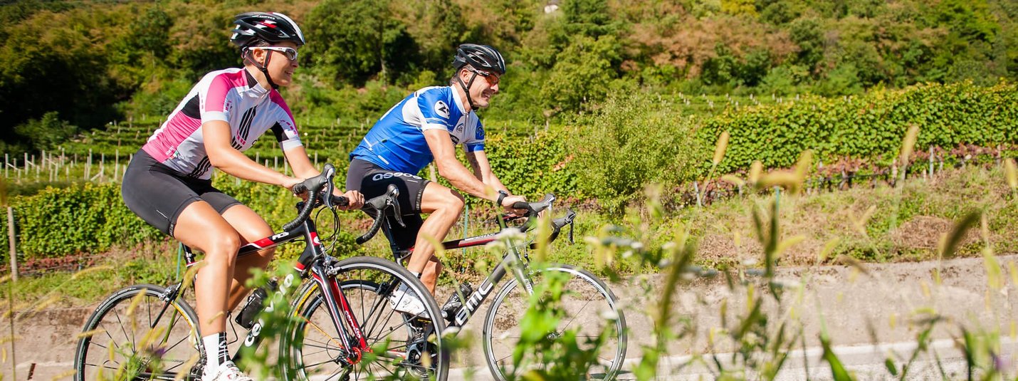 Rotaliana Tour Zwei Radfahrer in Mountainlandschaft fahren auf Straße entlang grüner Vegetation