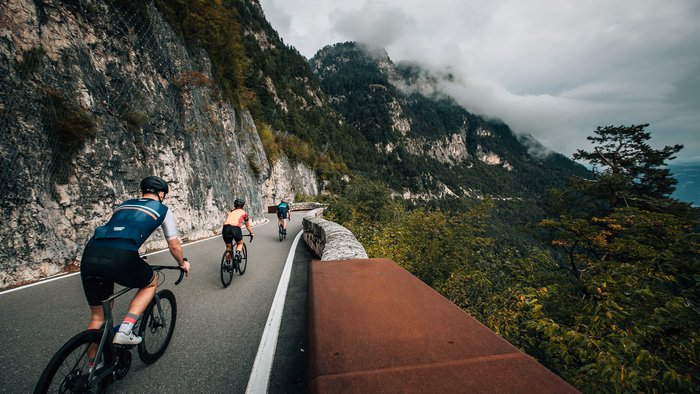 Tre ciclisti su una strada di montagna accanto a una parete rocciosa