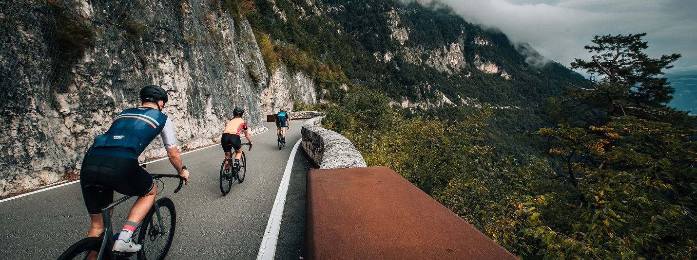 Tre ciclisti su una strada di montagna accanto a una parete rocciosa