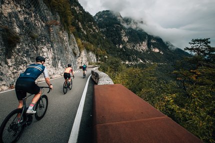 Drie fietsers rijden op een bergweg langs een rotswand