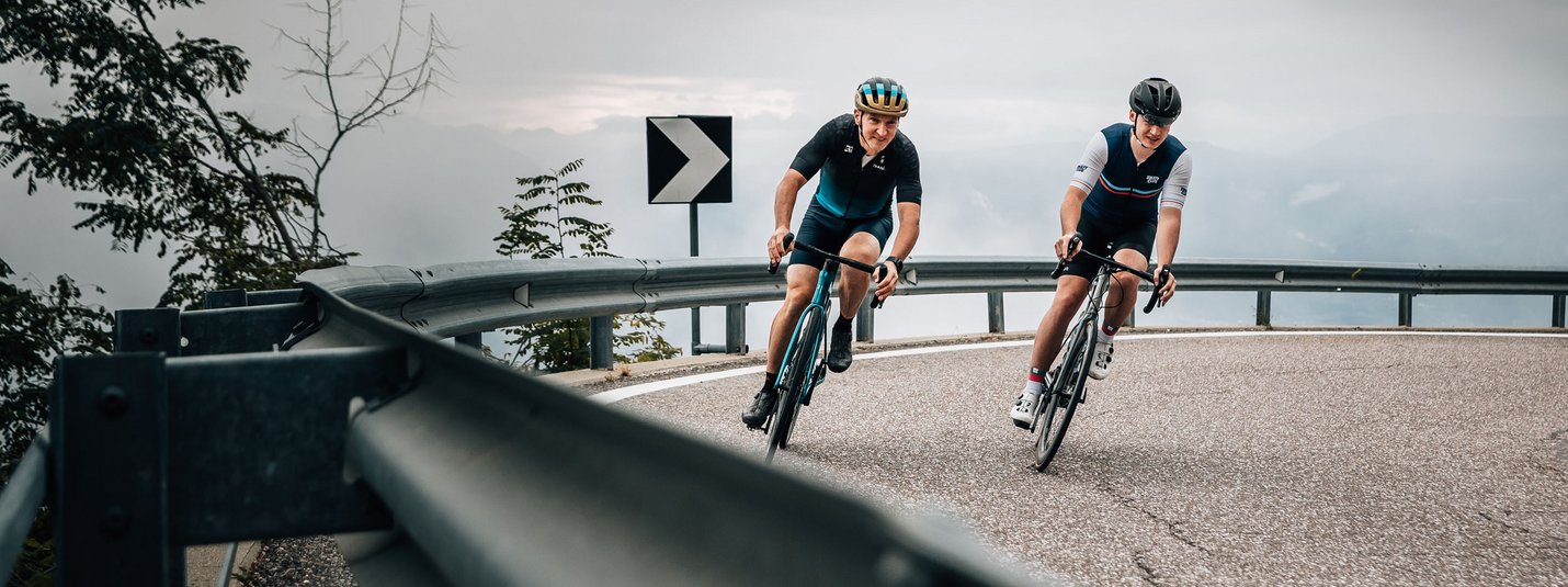 Twee wielrenners dalen een kronkelende bergweg af bij bewolkte lucht