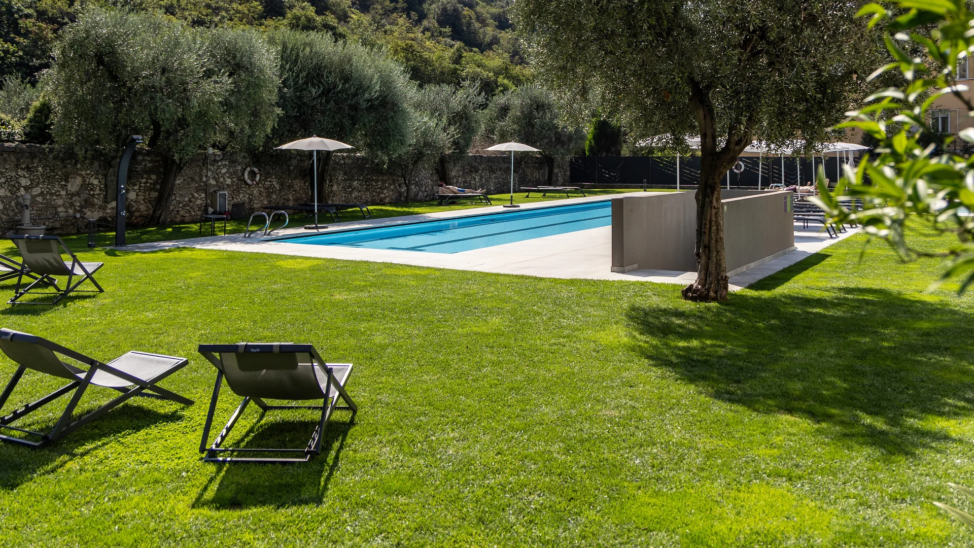 Dolce Vita tanken im AktivHotel Santa Lucia © Fabio Staropoli Liegestühle und grüner Rasen neben Schwimmbad in Berglandschaft bei Sonnenschein