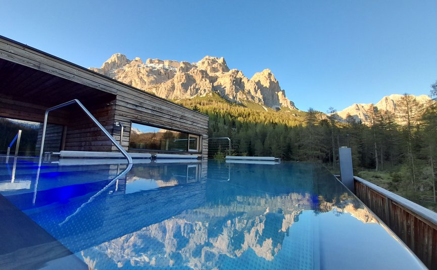 Infinity-Pool mit Bergblick und Holzhaus bei klarem Himmel