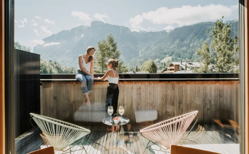 Zwei Frauen unterhalten sich auf einem Balkon mit Bergblick bei Sonnenschein