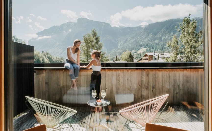 Riders Life Package Zwei Frauen unterhalten sich auf einem Balkon mit Bergblick bei Sonnenschein