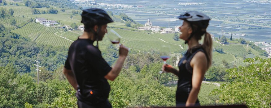 Zwei Radfahrer trinken Wein mit Blick auf grüne Weinberge und Berge