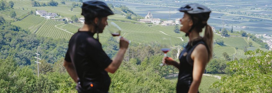 Zwei Radfahrer trinken Wein mit Blick auf grüne Weinberge und Berge