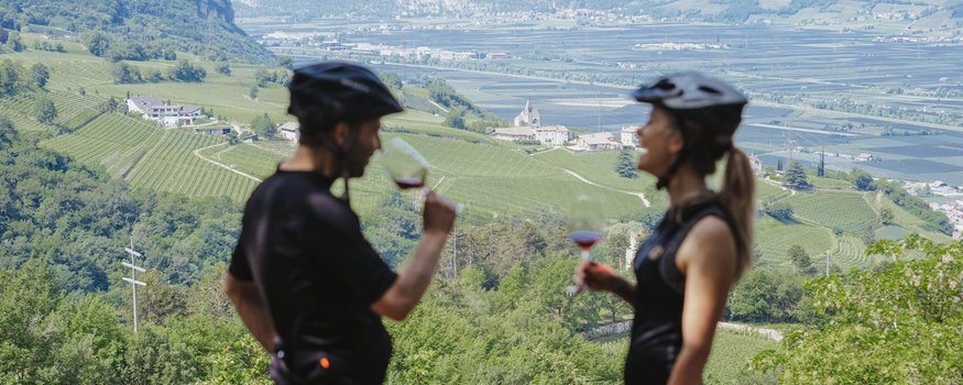 Zwei Radfahrer trinken Wein mit Blick auf grüne Weinberge und Berge