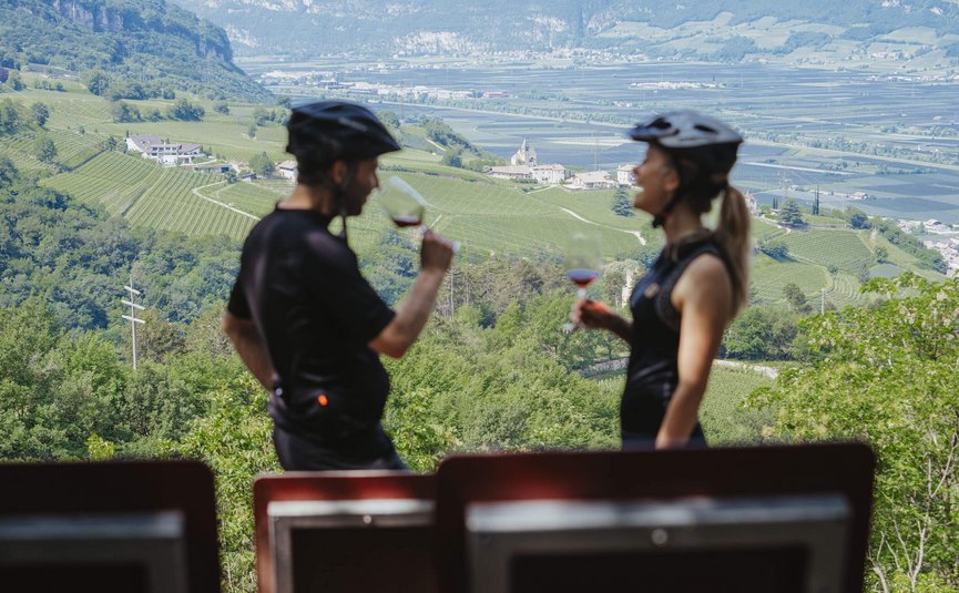 Due ciclisti che bevono vino con vista su vigneti verdi e montagne