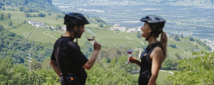 Due ciclisti che bevono vino con vista su vigneti verdi e montagne