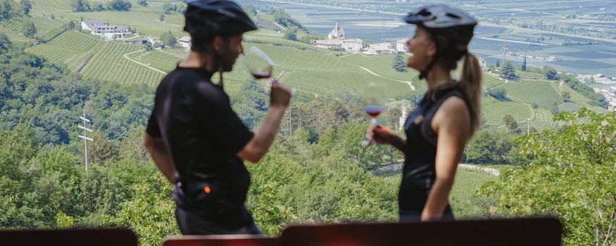 Zwei Radfahrer trinken Wein mit Blick auf grüne Weinberge und Berge