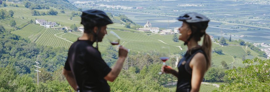 Zwei Radfahrer trinken Wein mit Blick auf grüne Weinberge und Berge