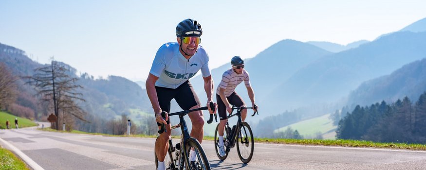 Zwei Rennradfahrer fahren auf einer Bergstraße bei sonnigem Wetter