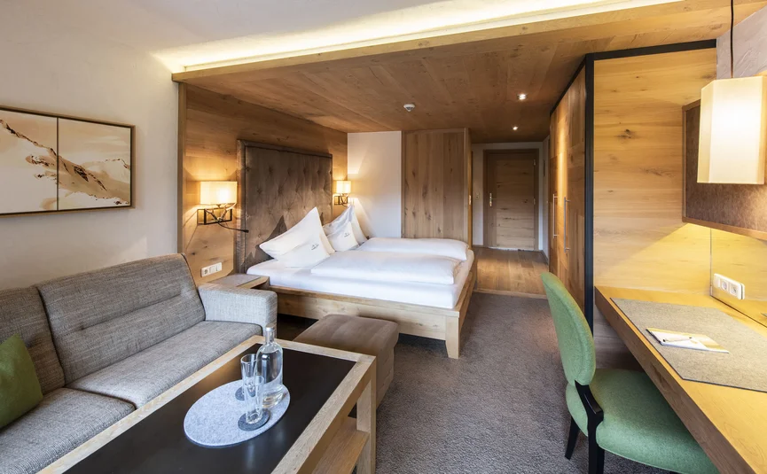 Gemütliches Hotelzimmer mit Bett, Sofa, grünem Stuhl und Holzmöbeln