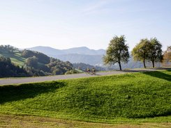 Two cyclists on a road in hilly landscape with trees and mountains