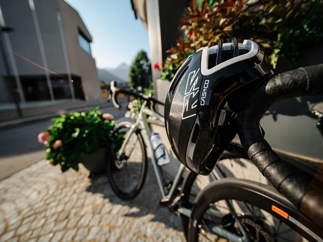 Fietshelm op racefiets stuur bij bloemen en stedelijke achtergrond met bergen